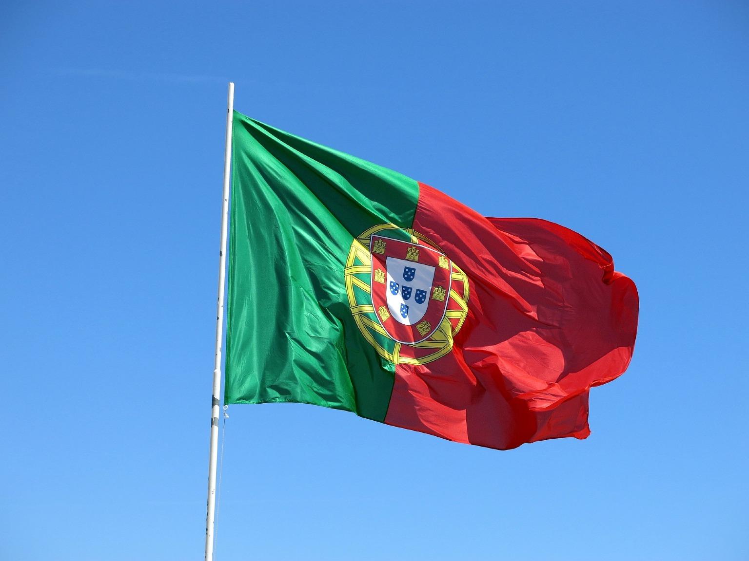 Bandeira de Portugal ondulando num fundo de céu azul. Celebração do Dia de Portugal e da unidade do povo português.