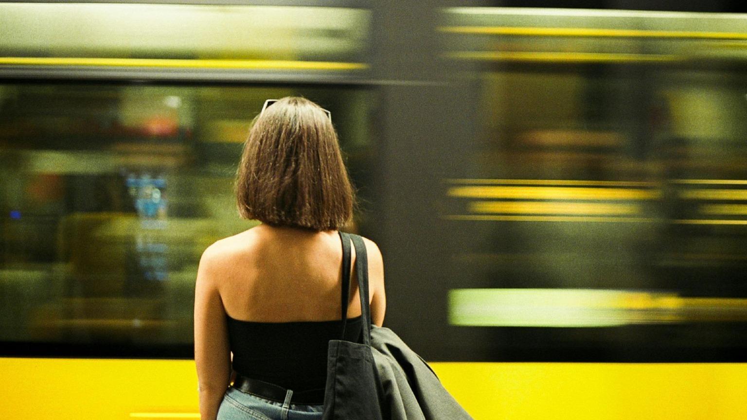A woman standing on the platform gazes at a Metro train passing by in Porto, Portugal