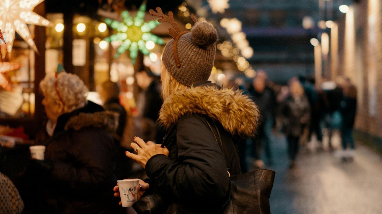 A woman buying gifts from a vendor at a Christmas market stall in Porto, Portugal.