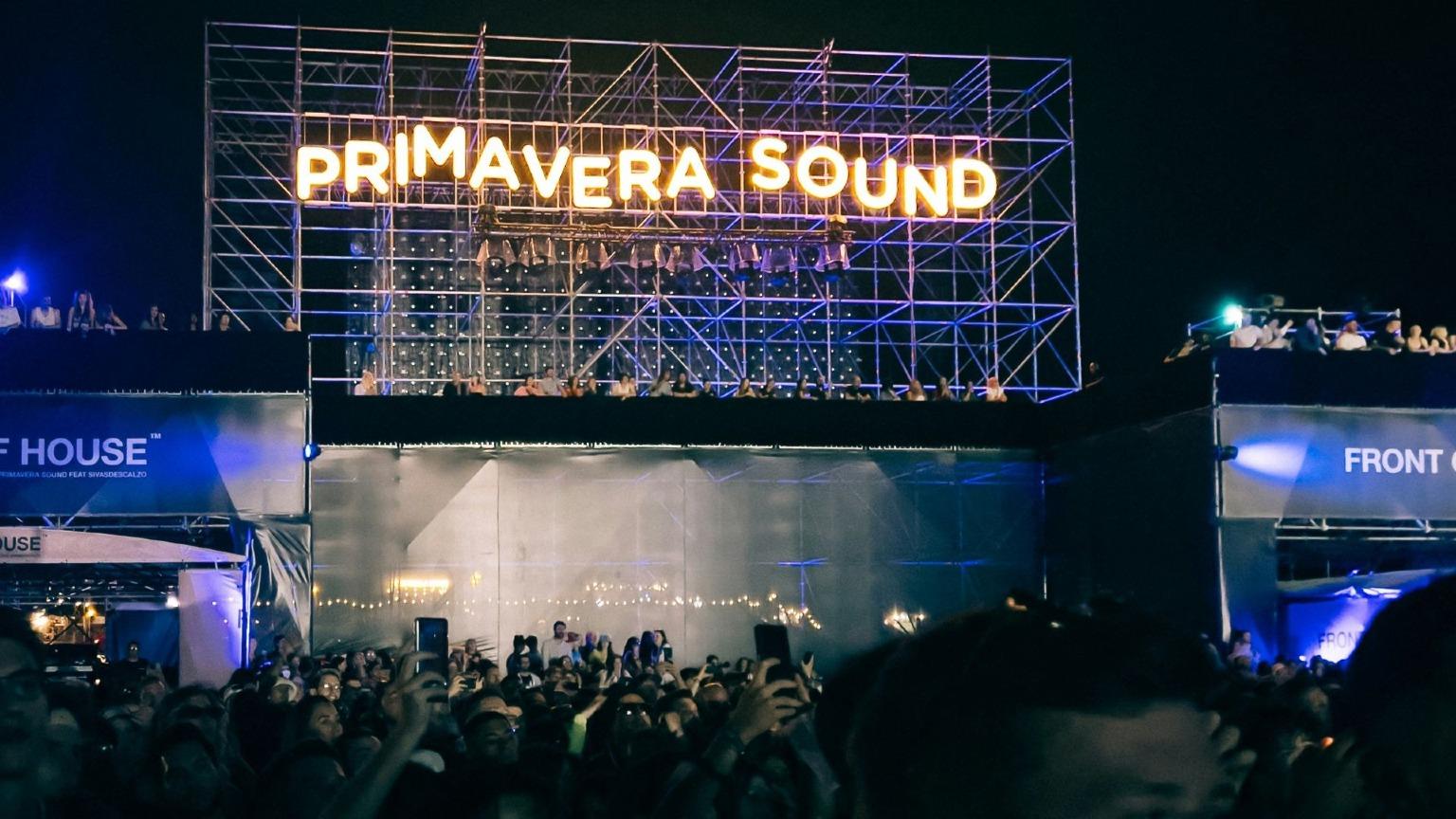 A vibrant scene of the Primavera Sound stage in Porto, illuminated with colorful lights as a large crowd of enthusiastic festival-goers enjoy the live performance at night.