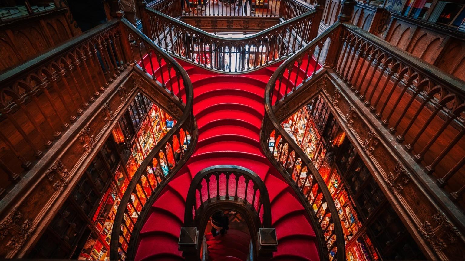 Suba a caprichosa escadaria vermelha da Livraria Lello, a icónica livraria do Porto, onde cada degrau ecoa uma história de encantamento literário e esplendor arquitetónico