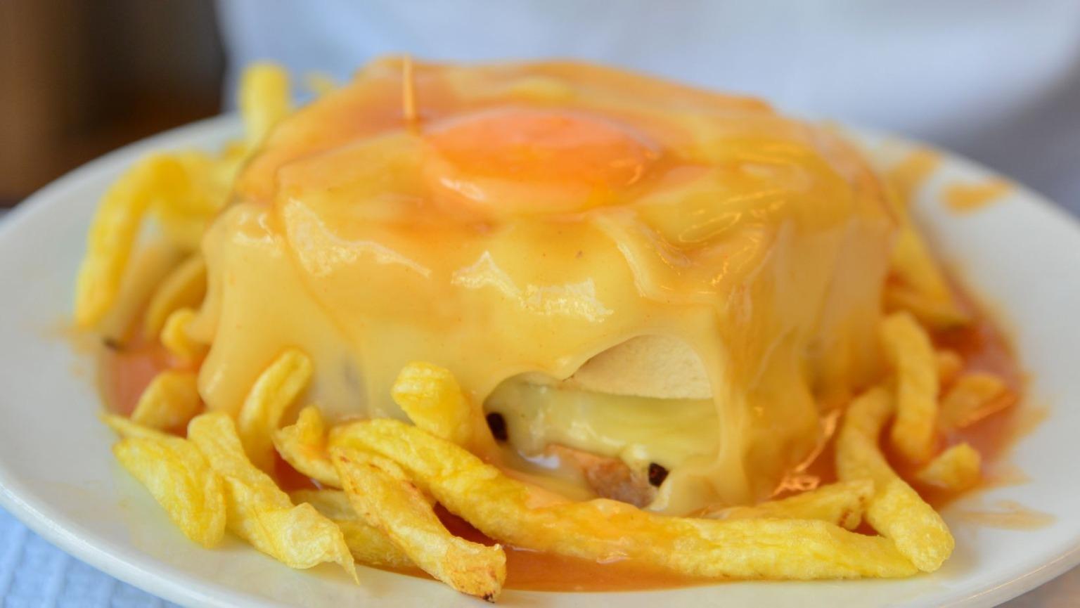 Um prato fervilhante com uma sanduíche de Francesinha de fazer crescer água na boca, coberta com queijo derretido, um ovo estrelado e coberta com um molho de tomate rico e picante.