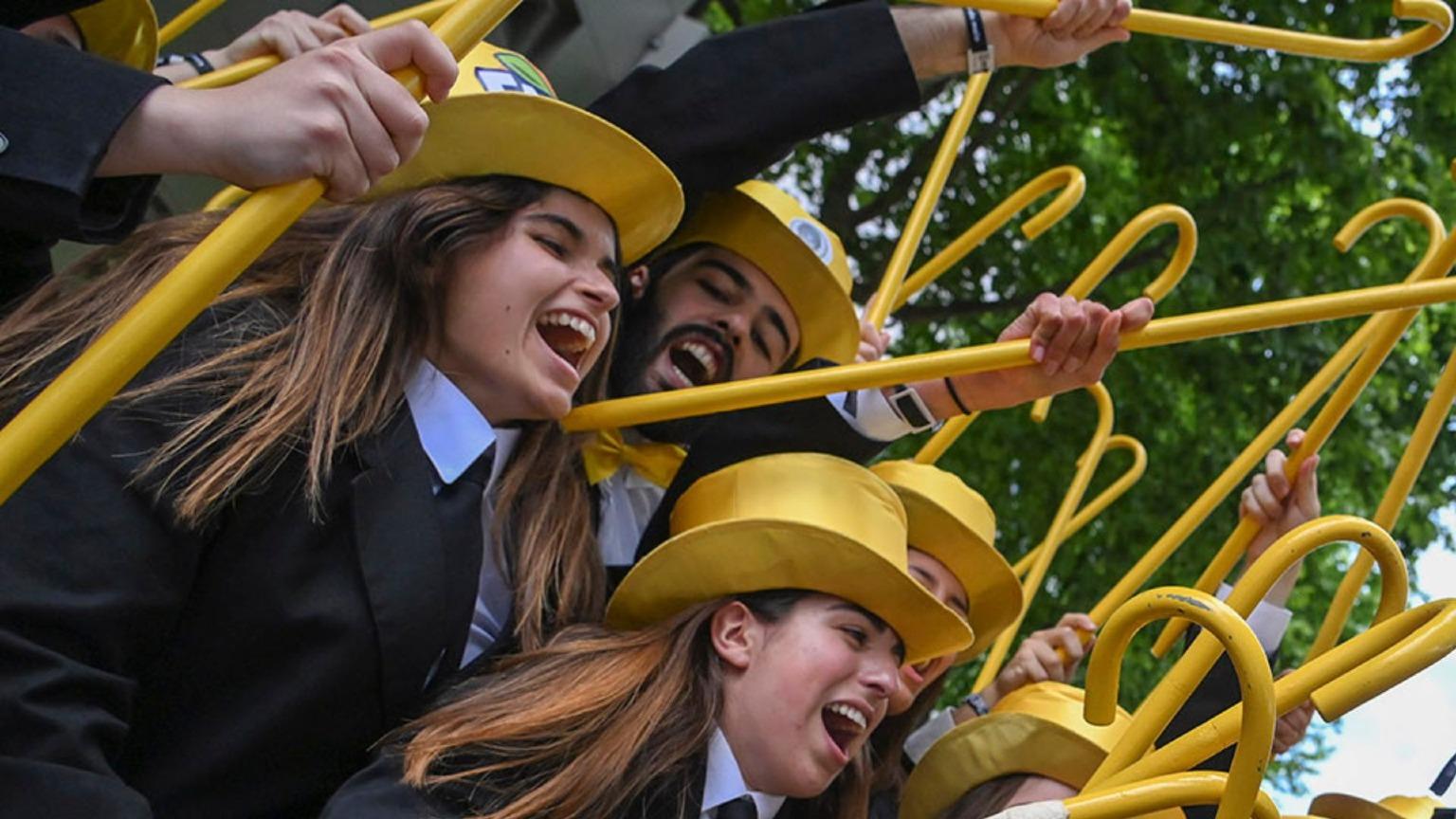 Students in traditional academic attire, wearing yellow hats and holding sticks, celebrate at Queima das Fitas in Porto