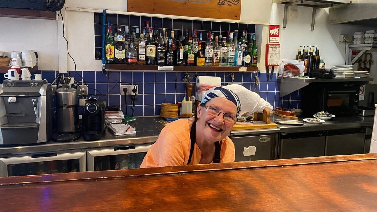 Chef local sorrindo atrás do balcão de uma taberna tradicional em Lagos