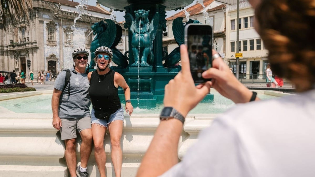 Guide prenant une photo d'un couple heureux près de la Fontaine des Lions à Porto lors d'une visite à vélo électrique des points historiques de la ville