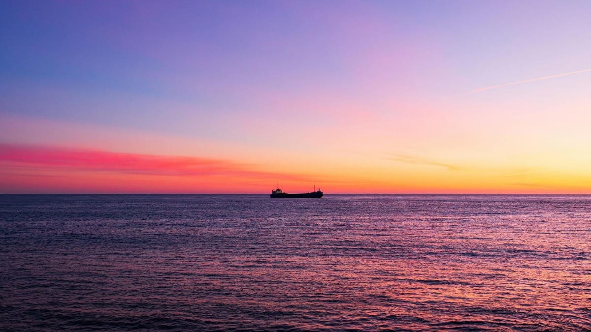 Magical sunset boat tour in Porto with a red and orange sky and a cargo ship in the distance