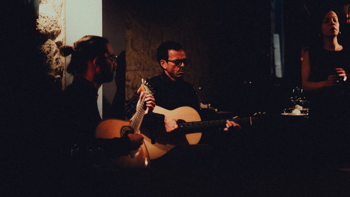 Dos guitarristas portugueses acompañando a una cantante de Fado que transmite emoción con su voz carismática