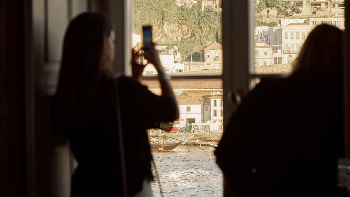 Person photographing the Douro River from the window of a Porto tasting room during sunset