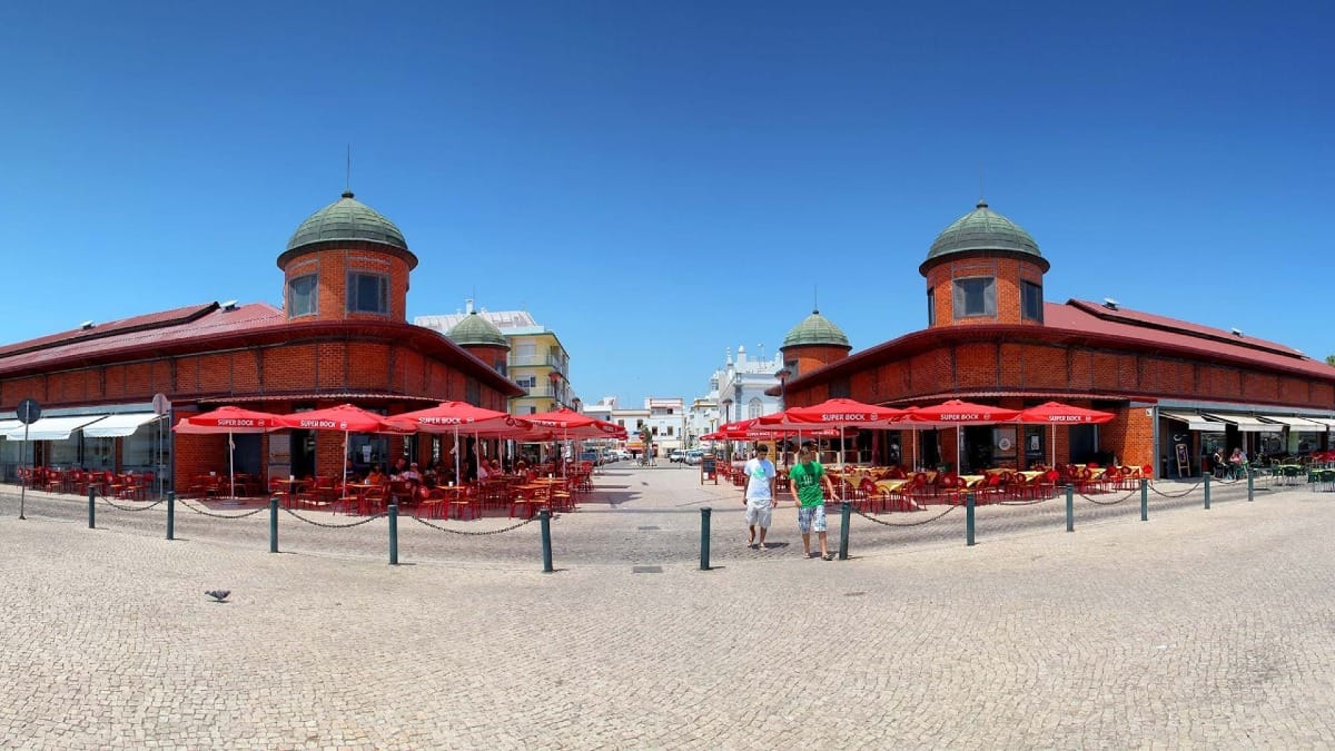 Fachada do Mercado Municipal de Olhão com arquitetura em tijolo vermelho e vendedores locais do lado de fora