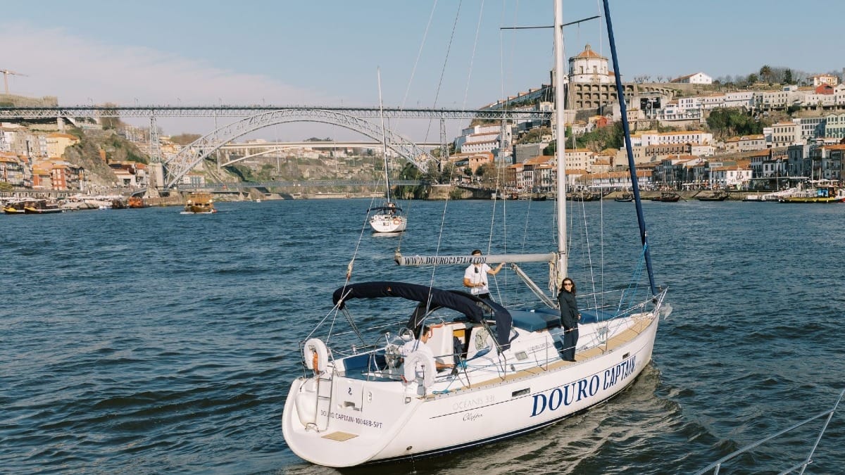 Invitados disfrutando un tour en velero soleado en Oporto con vistas panorámicas de la ciudad y el río