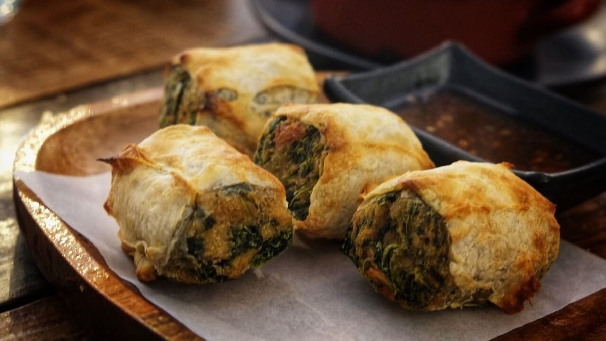 Rollitos de hojaldre rellenos de espinacas y salchicha servidos sobre bandeja de madera