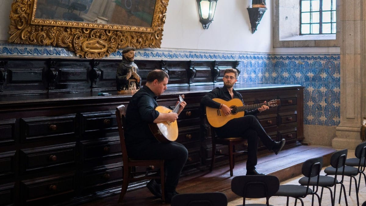 Musiciens accordant des guitares portugaise et classique à l'intérieur d'un monastère historique à Porto, Portugal, avec des azulejos en arrière-plan