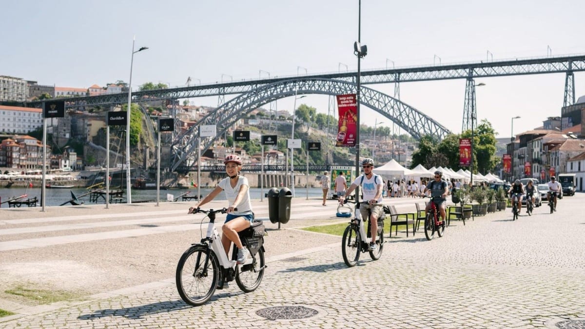 Porto electric bike tour along Gaia riverfront, with a small group cycling past historic Port wine cellars