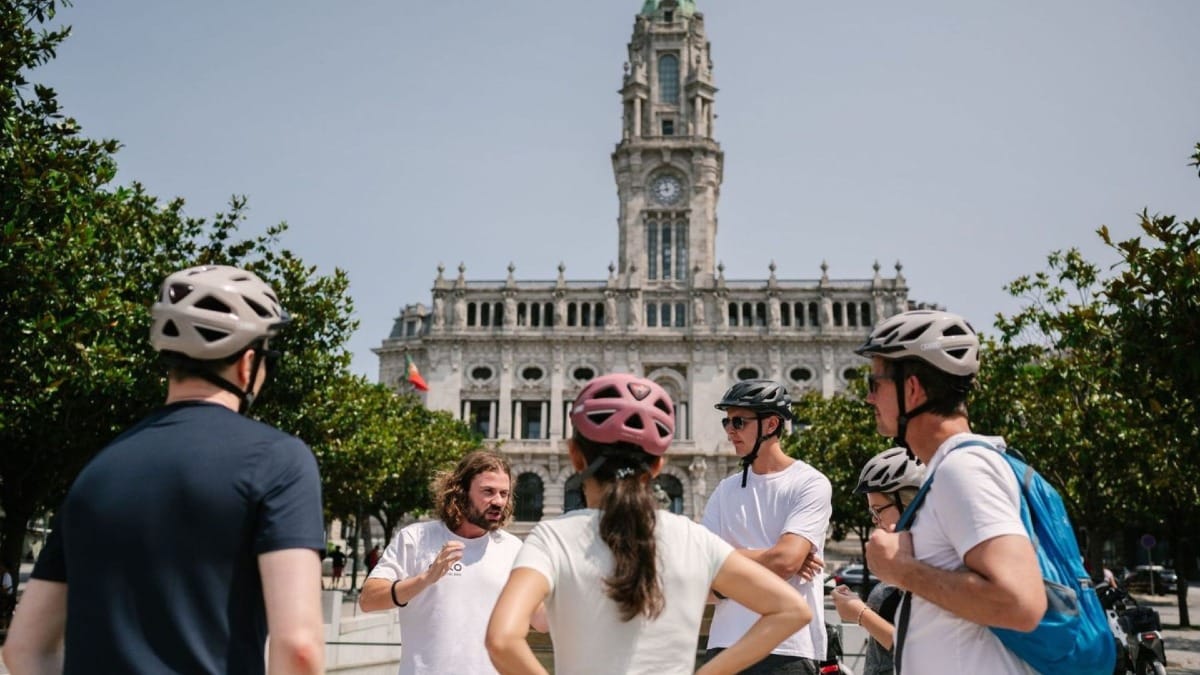 Guide racontant l'histoire de l’Avenida dos Aliados et de l'Hôtel de Ville de Porto à un petit groupe lors d'une visite à vélo électrique des points historiques de la ville