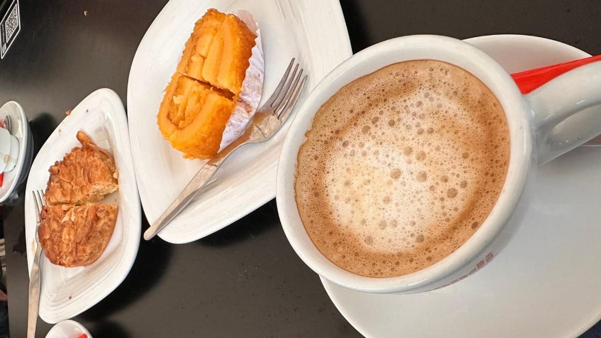 Taza de café portugués servida con tarta de almendras y pastel regional de huevo en platos blancos