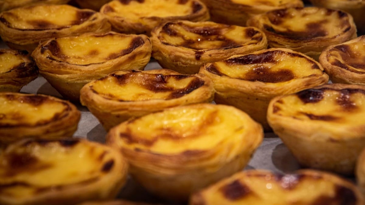 Pastéis de nata acabados de sair do forno com topo caramelizado em destaque numa pastelaria tradicional