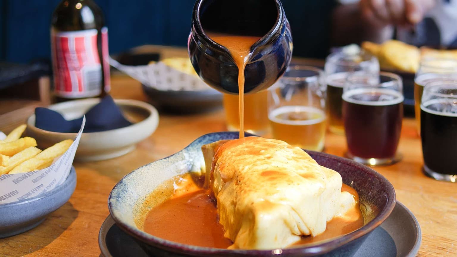 Salsa de francesinha vertiéndose sobre el famoso sándwich de Oporto durante un tour gastronómico por Oporto