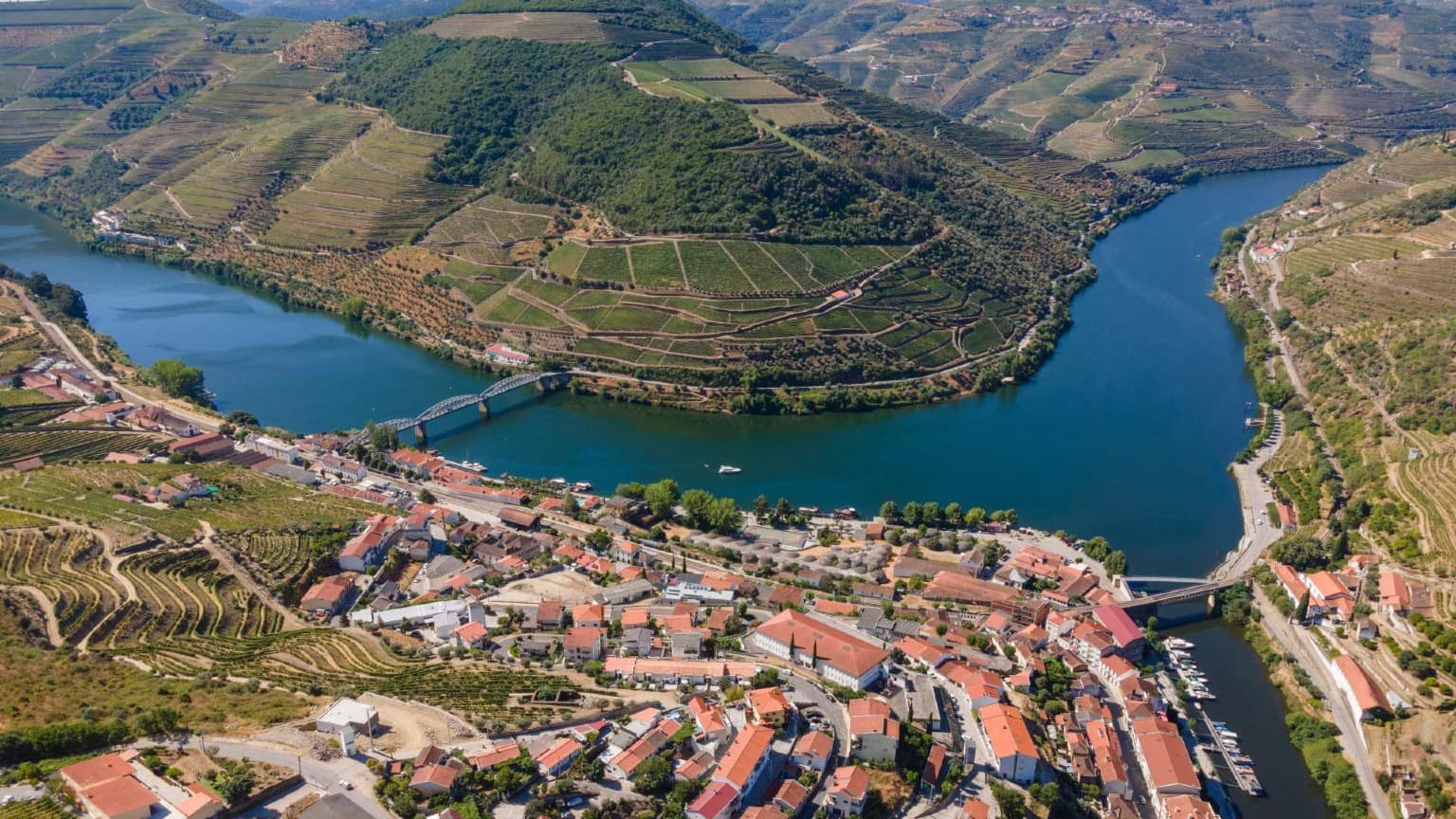 Vista aérea da aldeia de Pinhão no Vale do Douro, com casas de telhados vermelhos, vinhas circundantes e o rio Douro