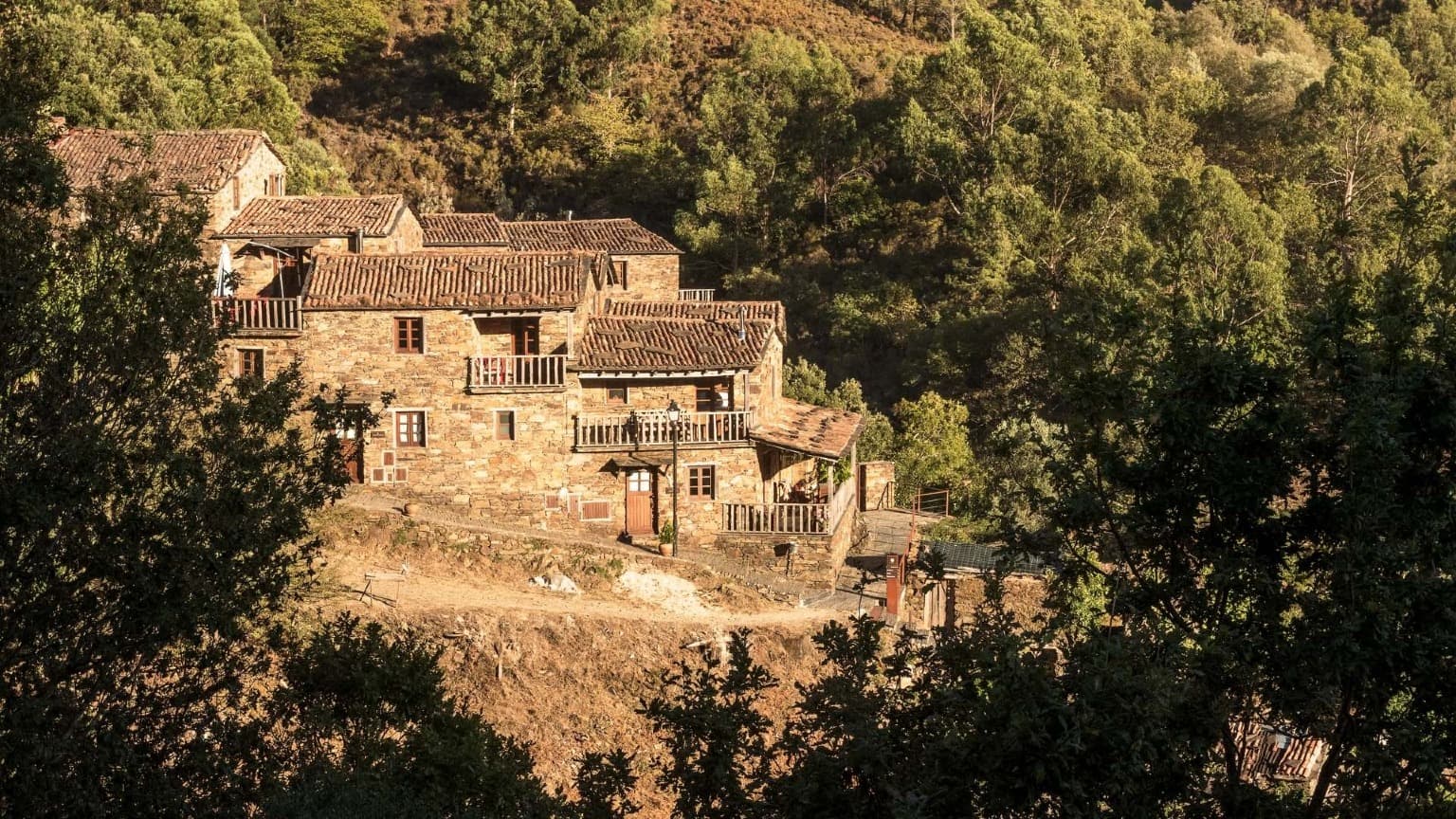 Casas de pedra numa aldeia tradicional de xisto perto de Lousã, rodeadas por colinas arborizadas no centro de Portugal.