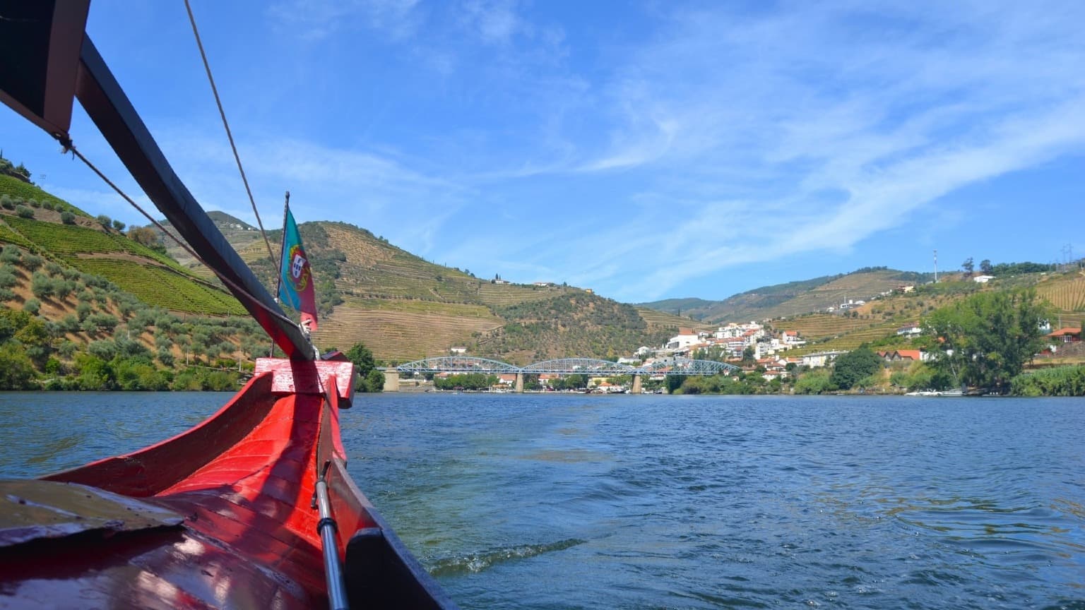 Barco rabelo tradicional de madeira no rio Douro, com as vinhas e a ponte do Pinhão ao fundo