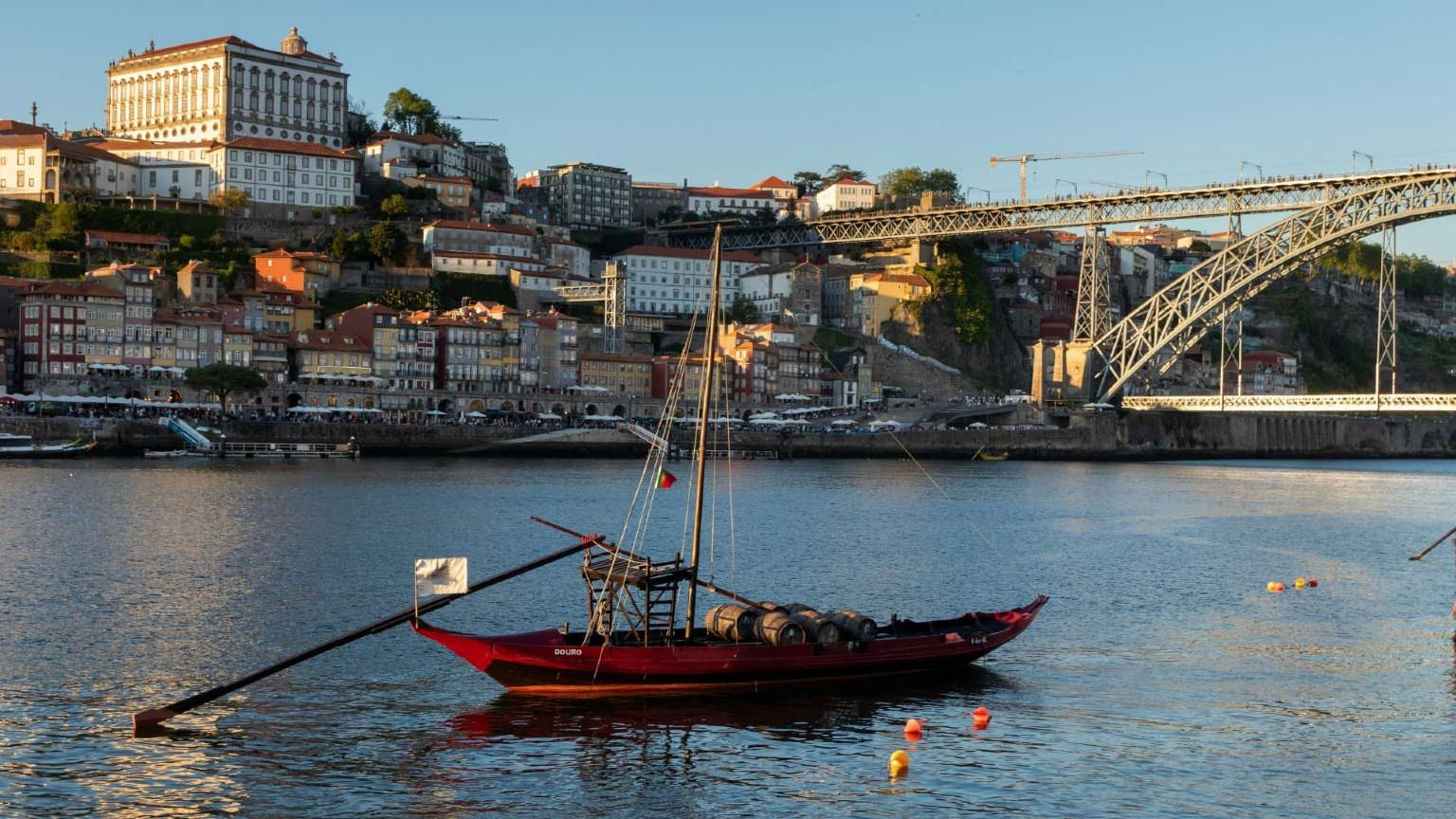 Barco rabelo no rio Douro, no Porto, com barris de vinho do Porto e a Ponte Dom Luís I ao fundo