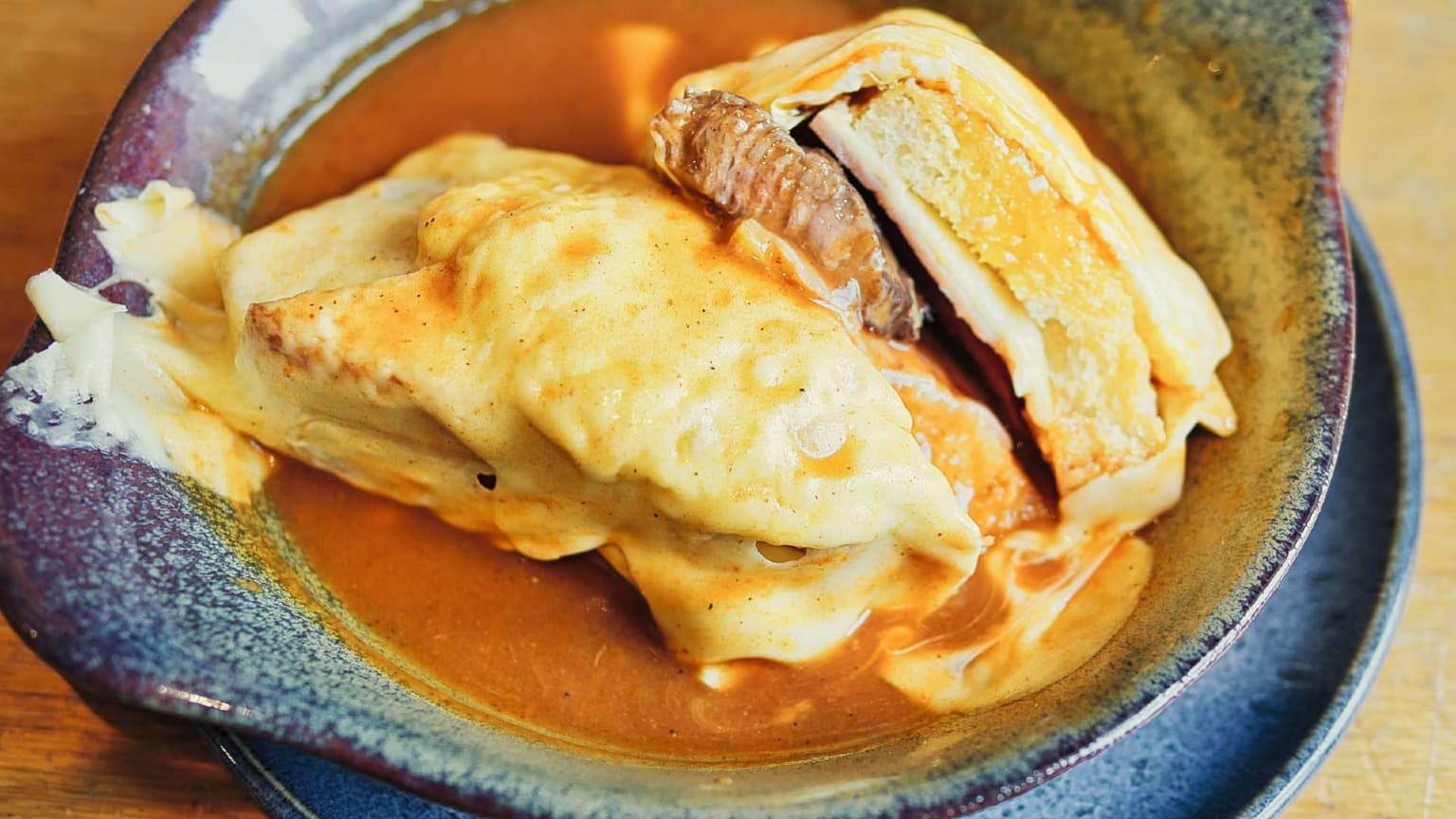 Grande plano da sanduíche de Francesinha mostrando camadas de carne, pão e queijo derretido