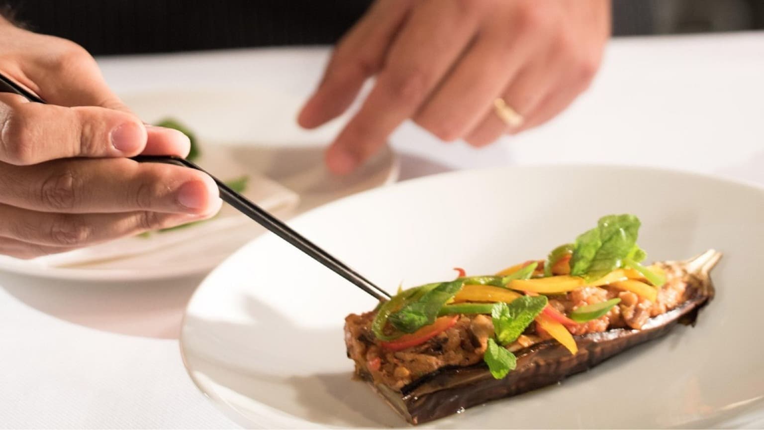 Um chefe dedicado a acrescentar cuidadosamente os últimos pormenores a um prato gourmet, realçando a precisão e a estética de uma refeição requintada.