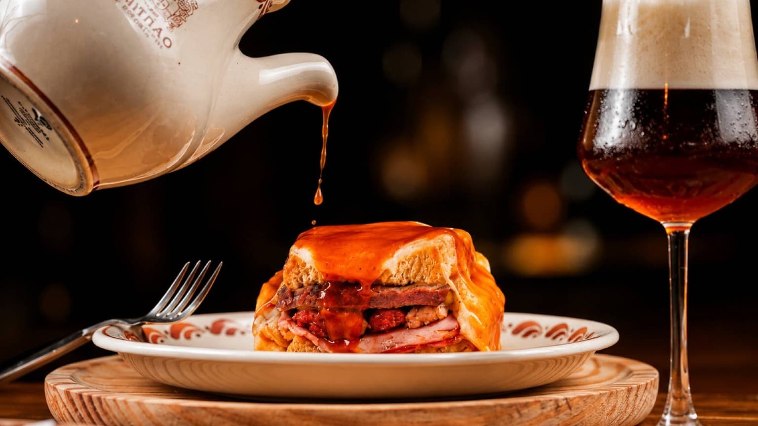 Oven-baked Francesinha served at Brasão Cervejaria in Porto with traditional sauce and Portuguese beer