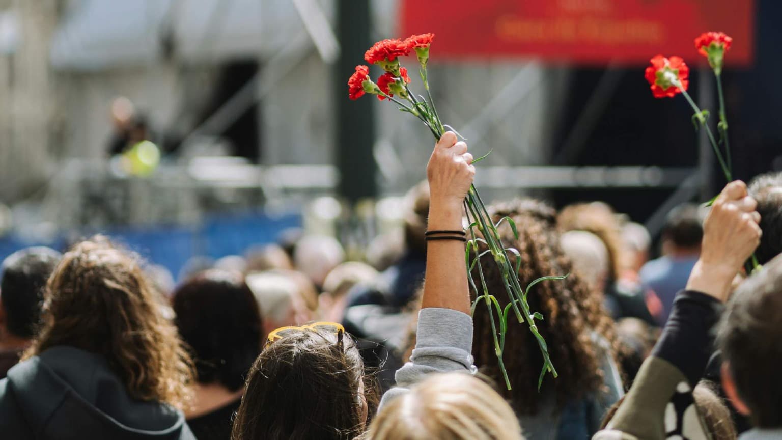Uma grande multidão reunida na Avenida dos Aliados no Porto nas celebrações do Dia da Liberdade a 25 de abril com vários cravos vermelhos erguidos no ar em frente a um palco de concerto