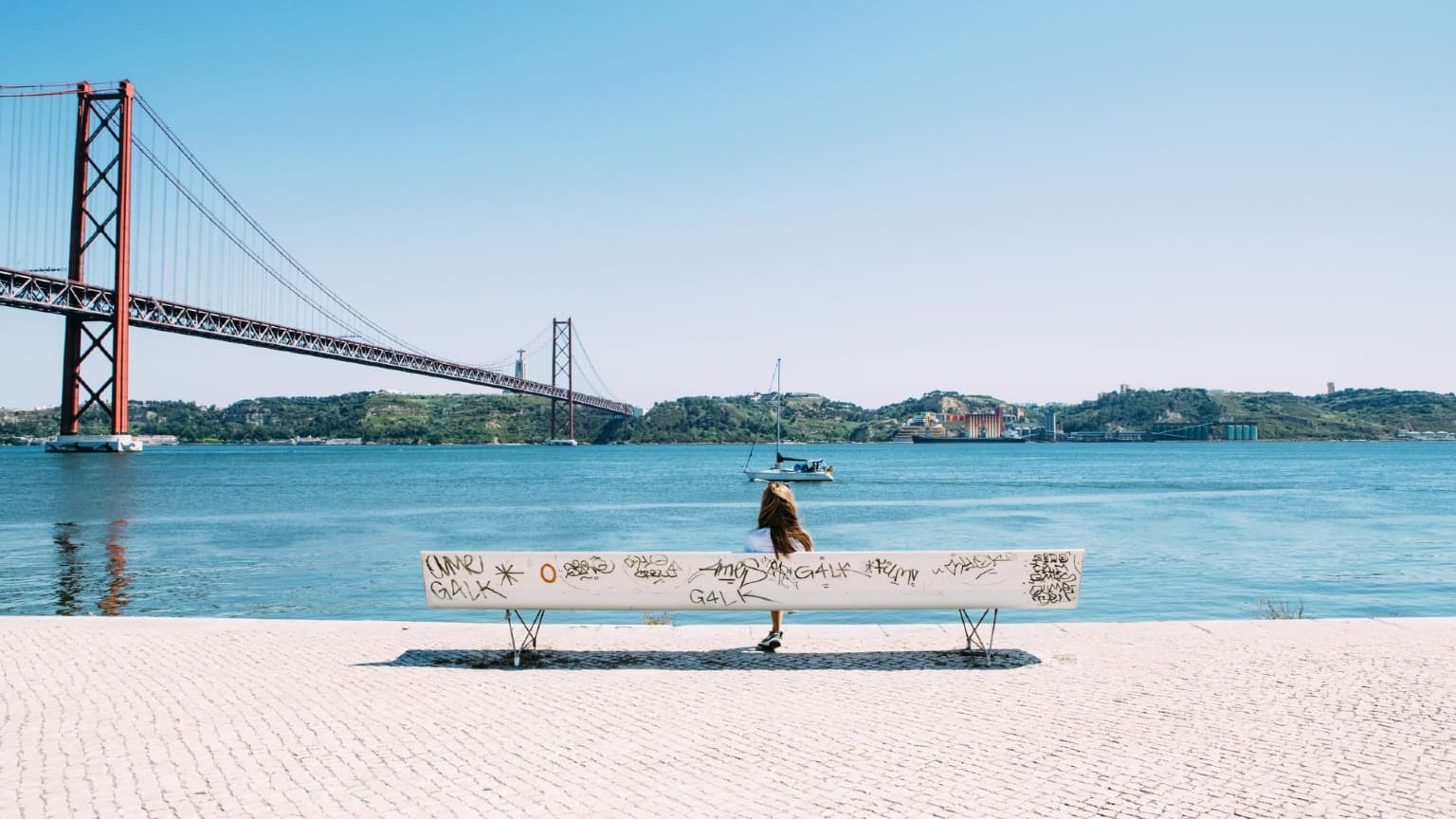 Banco no passeio ribeirinho do rio Tejo, com a Ponte 25 de Abril ao fundo