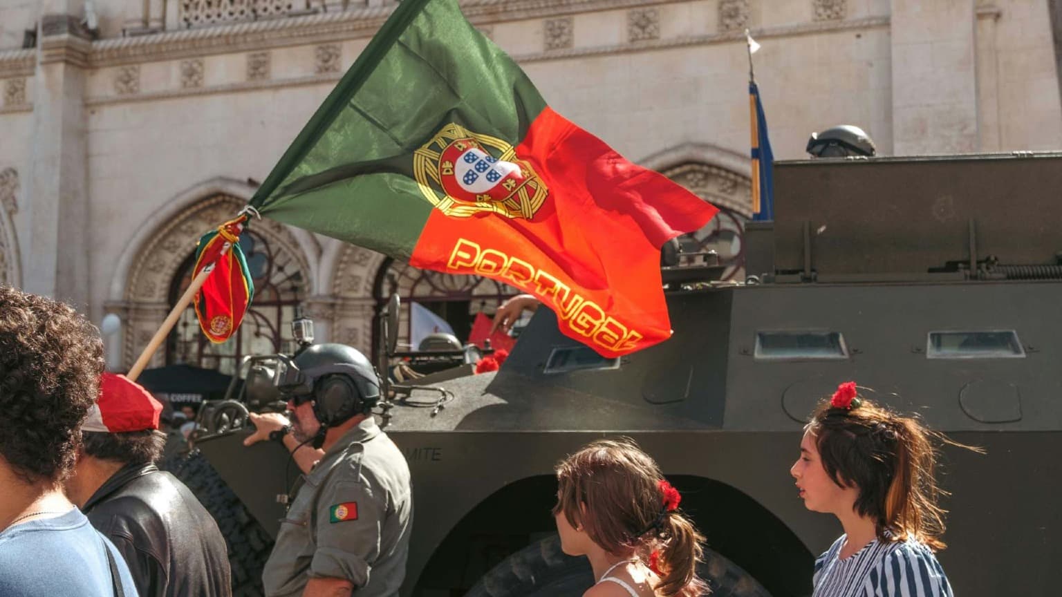 Bandeira portuguesa e civis junto a um veículo militar durante as comemorações da Revolução dos Cravos de 25 de abril, em Lisboa
