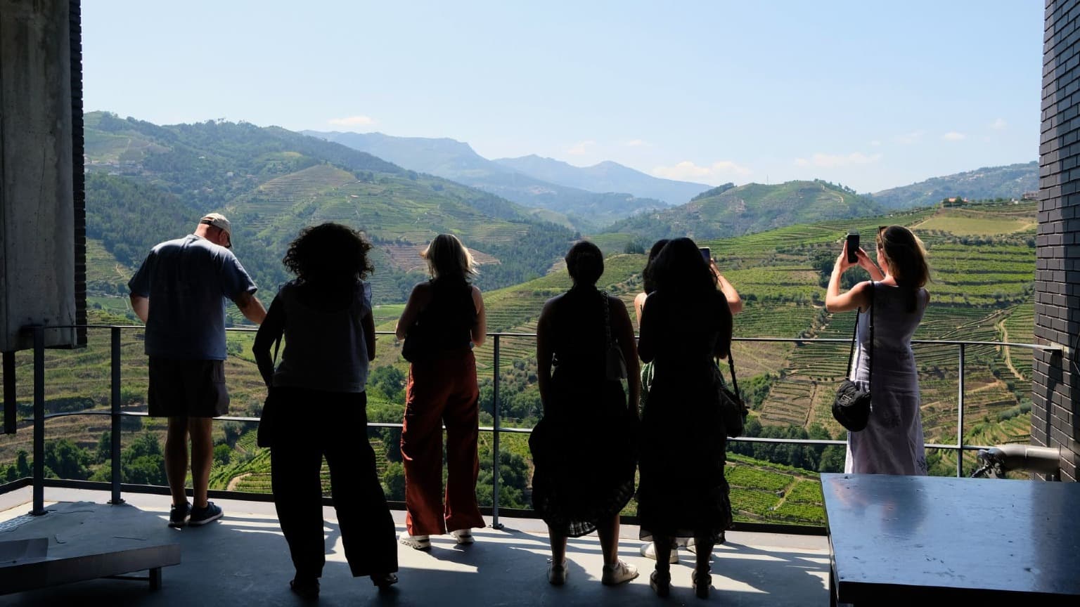 Grupo de turistas a admirar vistas panorâmicas sobre as vinhas em socalcos do Vale do Douro a partir da varanda de uma quinta vinícola