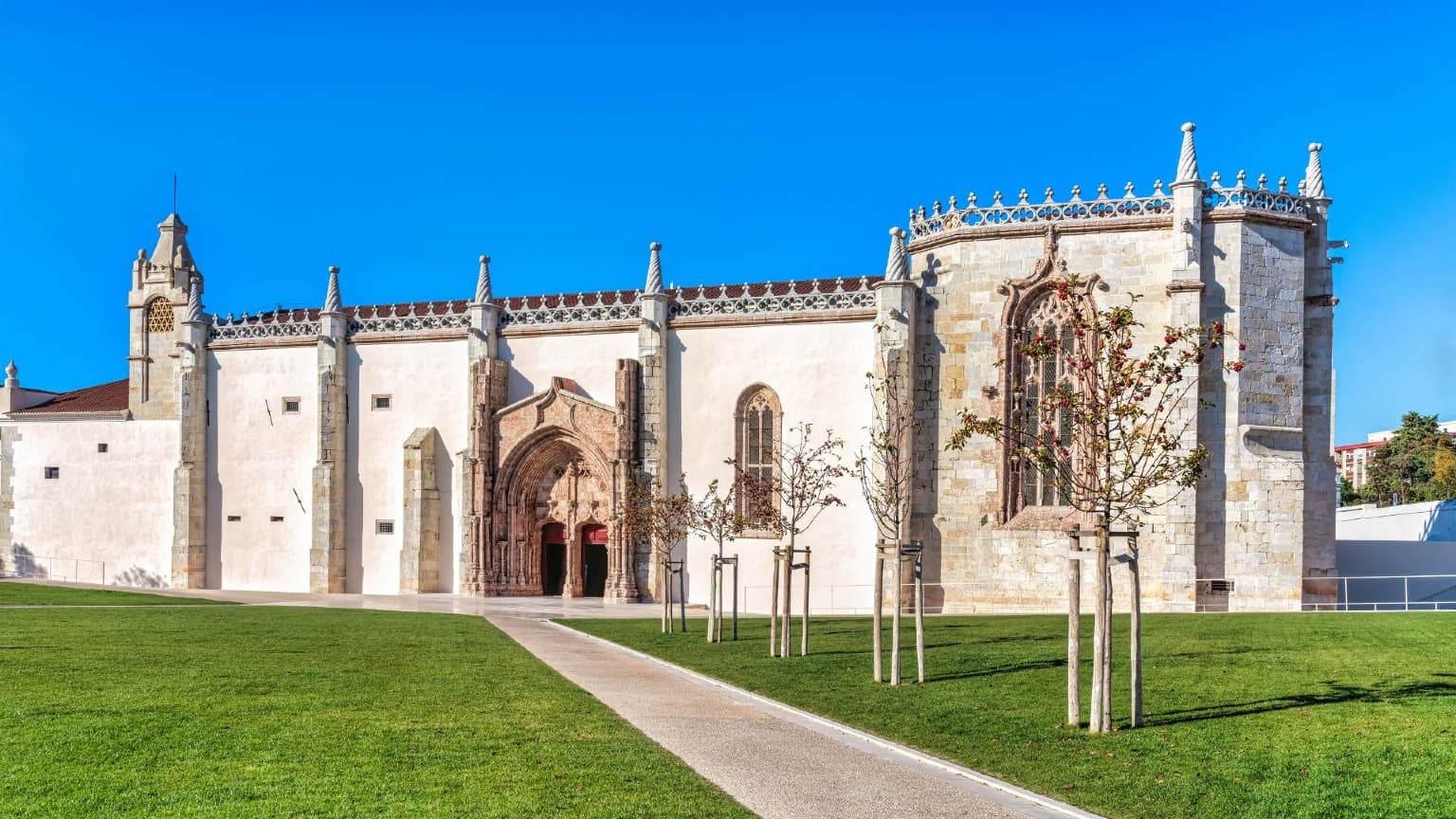 Vista exterior del Convento de Jesús en Setúbal con detalles góticos manuelinos, fachada de piedra y césped verde.