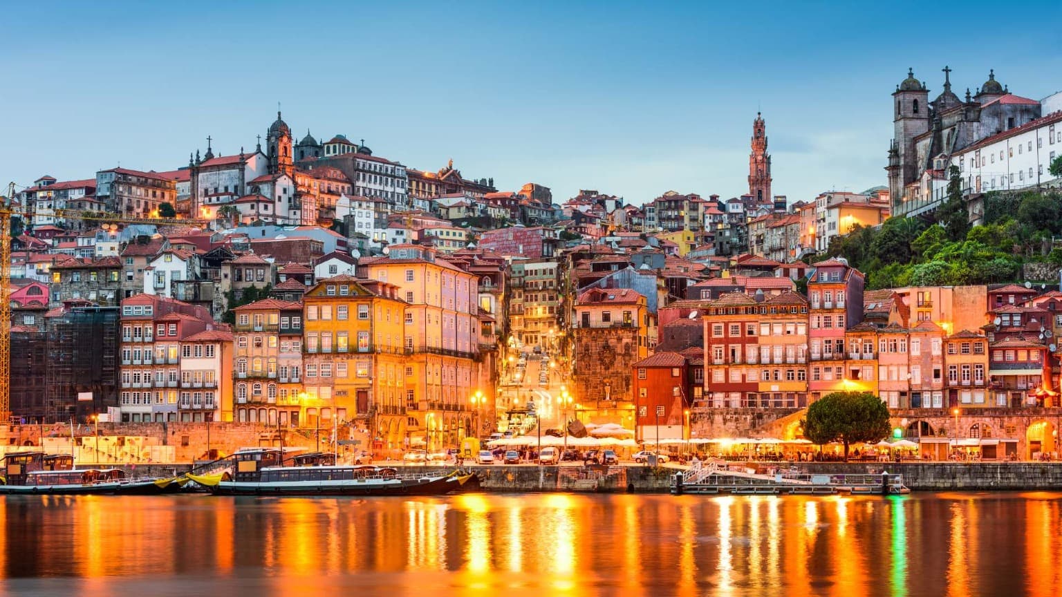Vista noturna do colorido bairro da Ribeira, no Porto, refletido no rio Douro, um cenário deslumbrante para os fogos de artifício de Ano Novo.