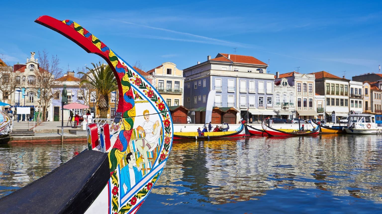 Proa pintada de colores de un moliceiro tradicional junto al canal de Aveiro y los edificios del paseo marítimo