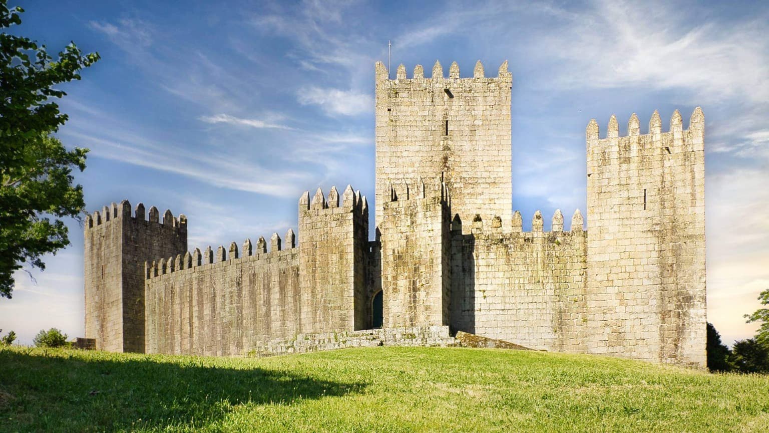Medieval Guimarães Castle with its tall stone walls and towers under a blue sky.