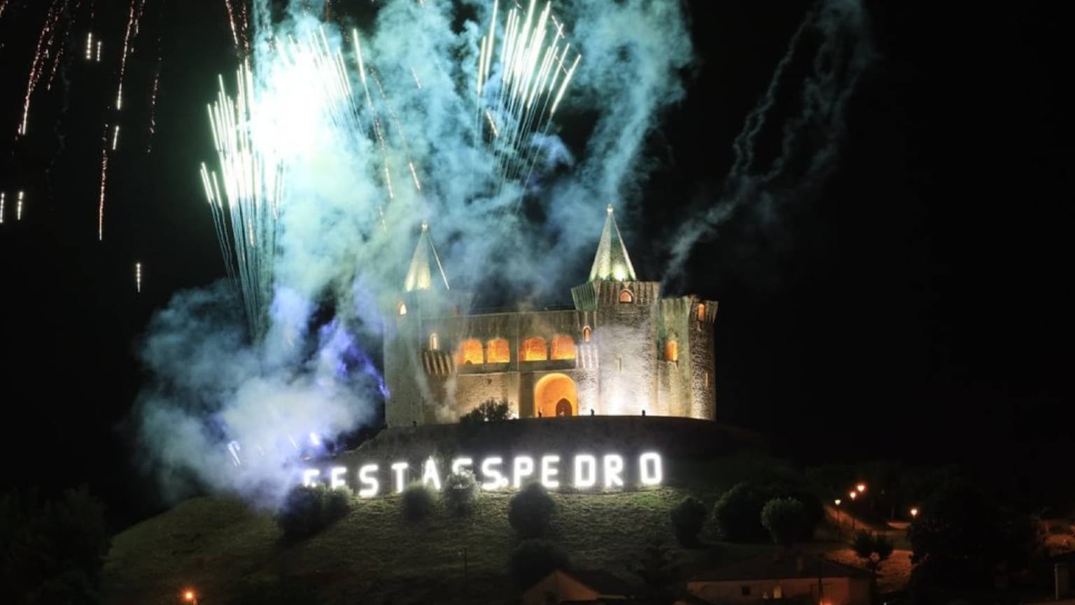 Fuegos artificiales sobre el castillo iluminado de Porto de Mós durante las Festas de São Pedro