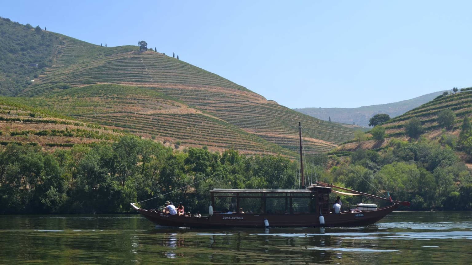 Barco tradicional rabelo a navegar no rio Douro perto de Pinhão, rodeado por colinas cobertas de vinhas no Vale do Douro