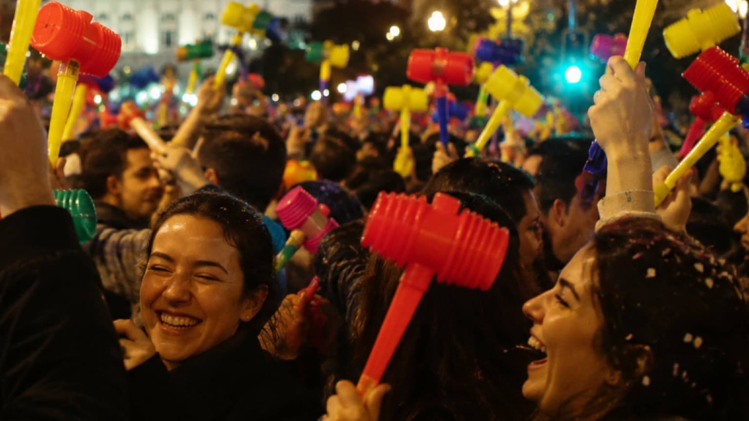 Multidão de pessoas segurando martelos de plástico coloridos durante as celebrações de rua das Festas de São João no Porto, à noite