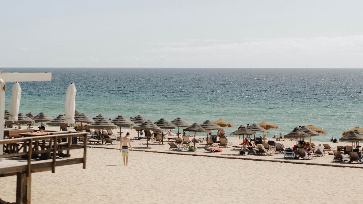 Praia da Comporta, en la región de Setúbal, con arena dorada, tumbonas, sombrillas de paja y el océano Atlántico.