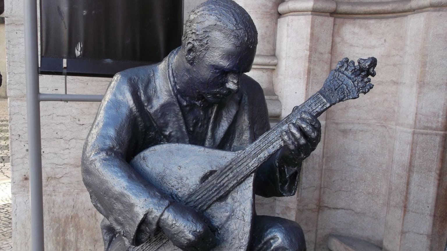 Estátua de bronze de um guitarrista de fado tocando a tradicional guitarra portuguesa em Lisboa, simbolizando a herança musical da cidade