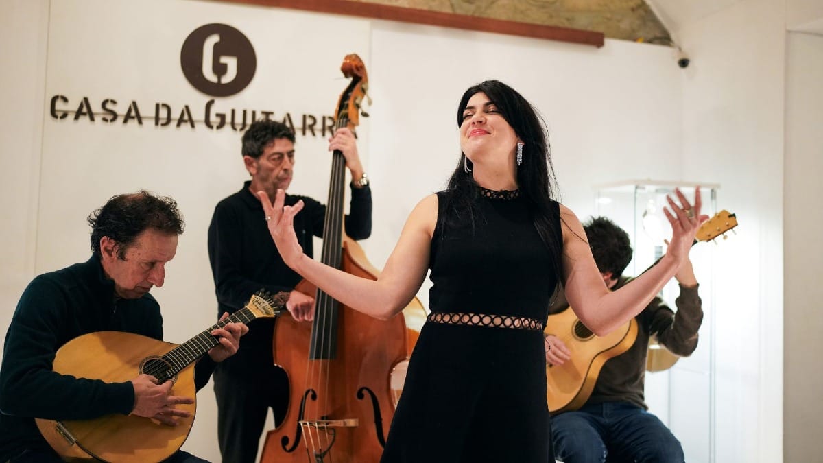 Female Fado singer with open arms and musicians playing in the background at Casa da Guitarra