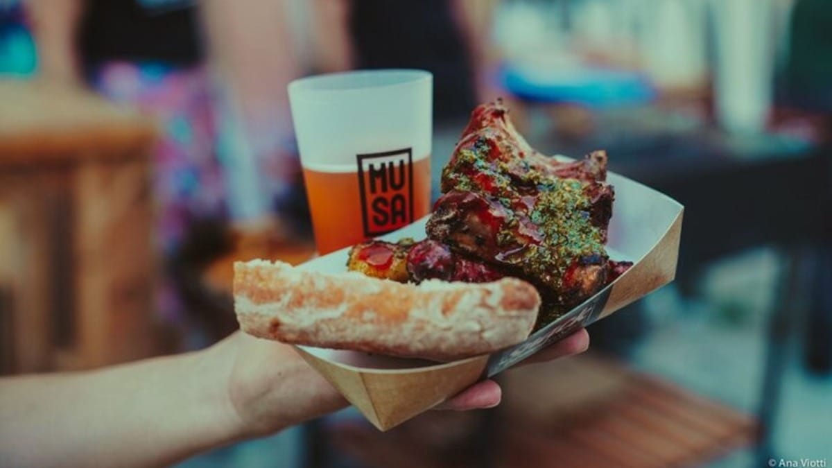 Mão segurando comida de rua com carne grelhada e cerveja artesanal local em Faro